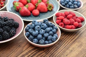 different fresh summer berries in bowls on wooden background closeup