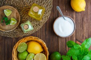 limes with lemons, herbs, drinks, salt in basket and plate on wooden and placemat background, flat lay.